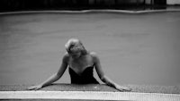 a black and white photo of a woman leaning against the edge of a pool