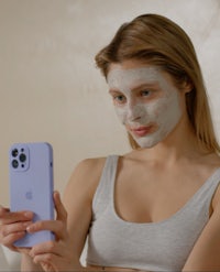 a woman with a facial mask on her face looking at her phone