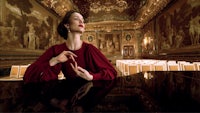 a woman sitting at a piano in an ornate room