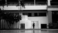 a black and white photo of a woman standing in front of a building